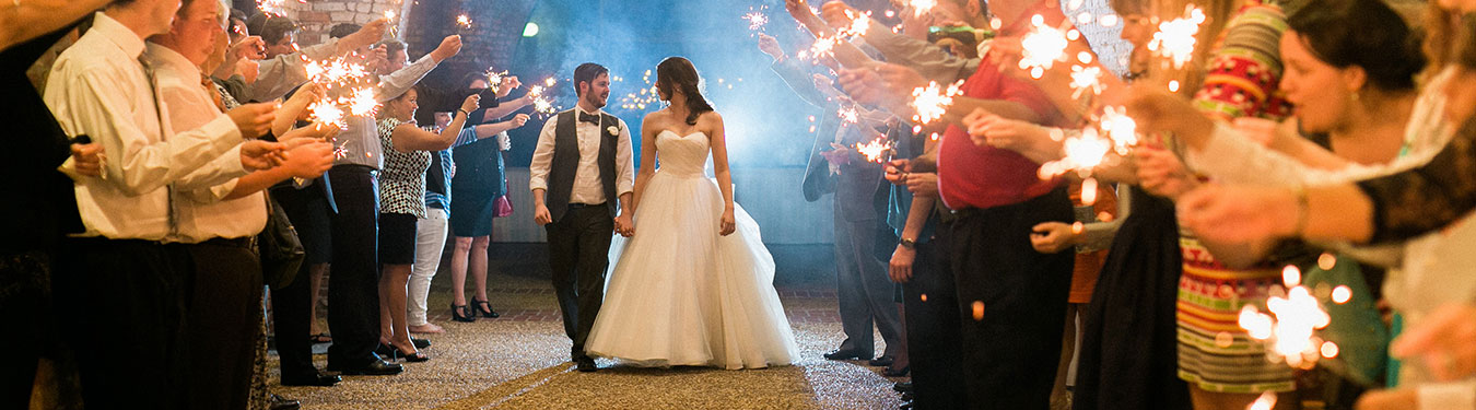 A man and a woman walking together with people holidng sparklers on either side