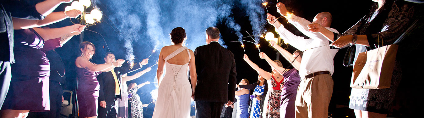 A man and a woman walking away from the camera with people holidng sparklers on either side